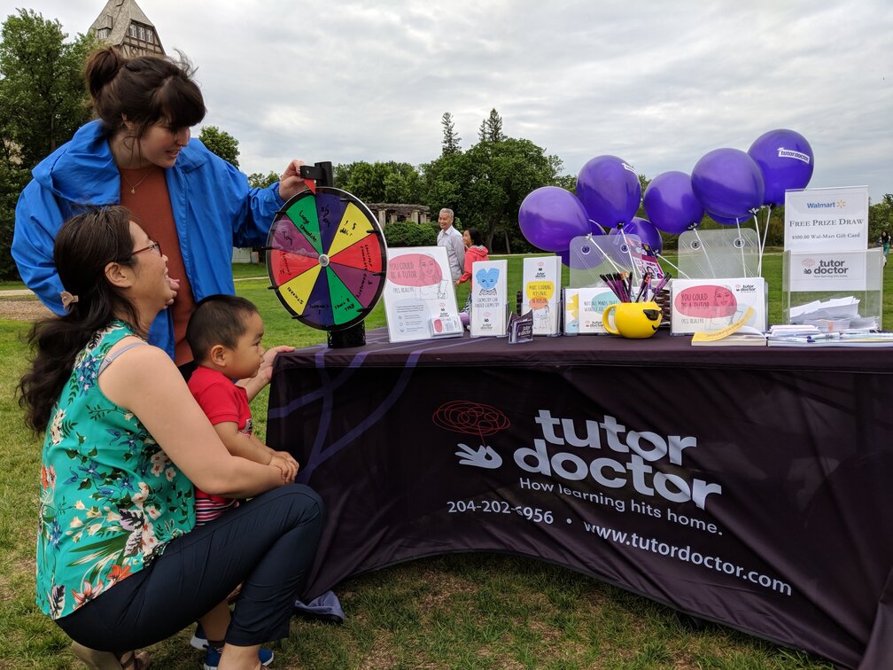 Two women and a child spinning a wheel at Tutor Doctor event table