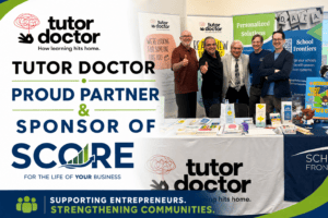 Five smiling men pose behind a Tutor Doctor and SCORE branded booth with promotional materials.