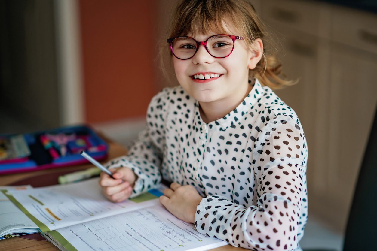 Young girl in glasses working through a workbook at her desk at home