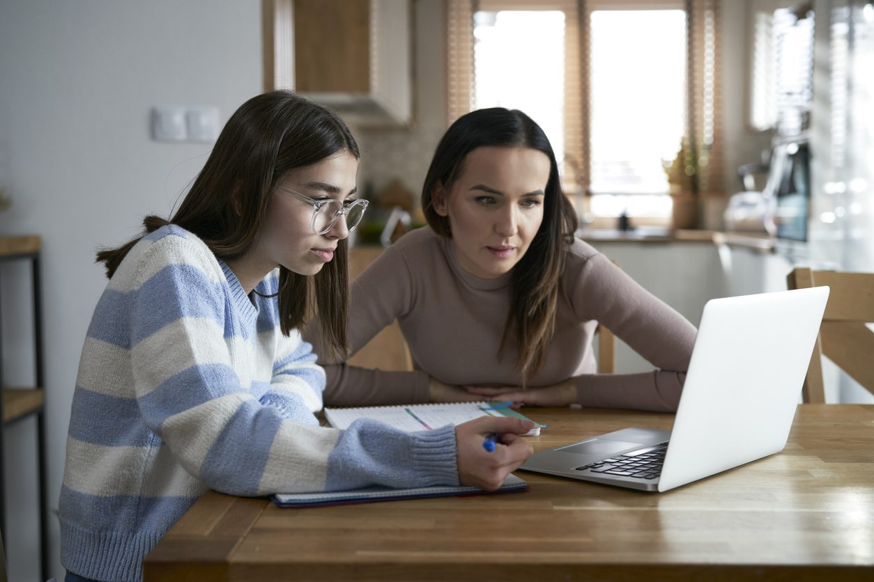 Teenage girl and an adult reviewing schoolwork together on a laptop at the kitchen table