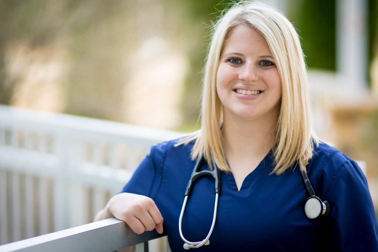 Nursing student in blue scrubs with a stethoscope smiling outdoors