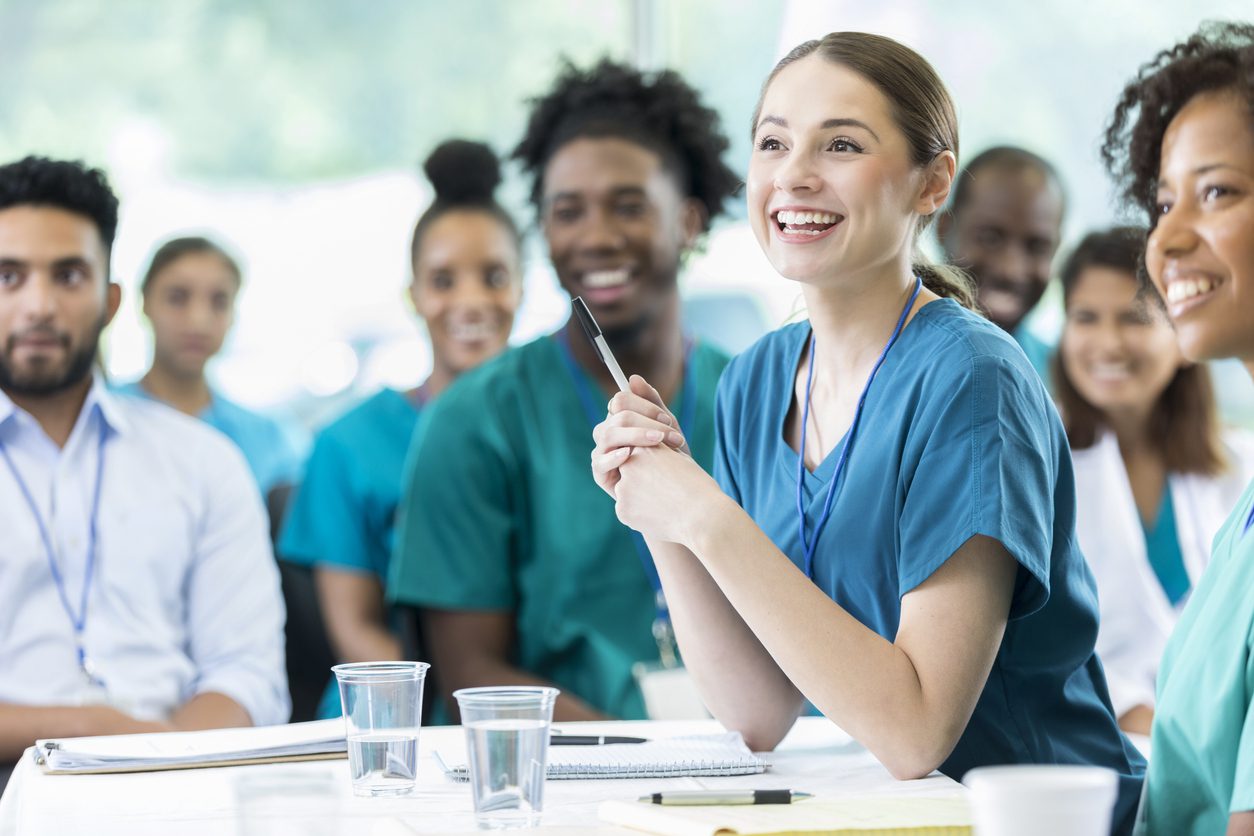 Nursing students listening during a class session, one holding a pen