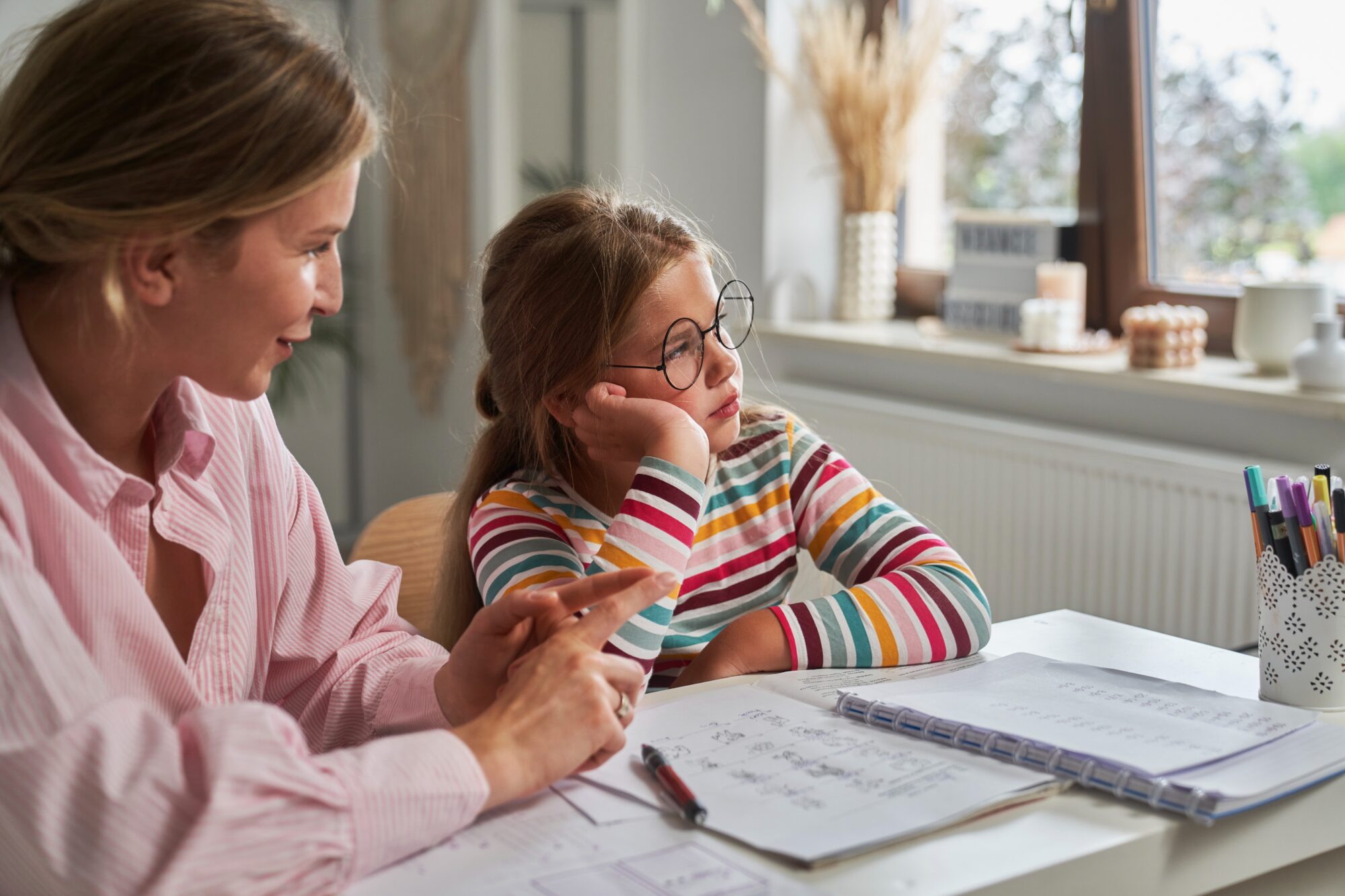 A mother sitting beside her daughter, supporting her with homework at a desk