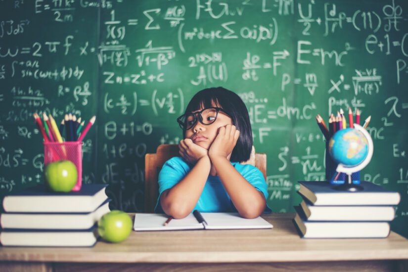 Student sits in classroom with math on blackboard behind them